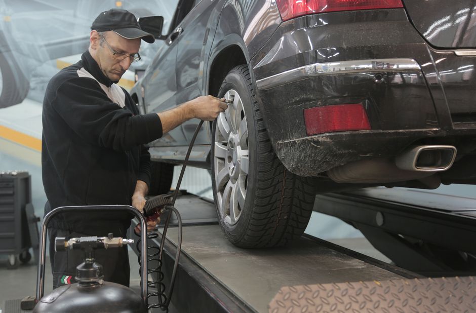 Side view of professional serious auto mechanic in casual uniform and eyeglasses pumping up car wheel while working in modern car service