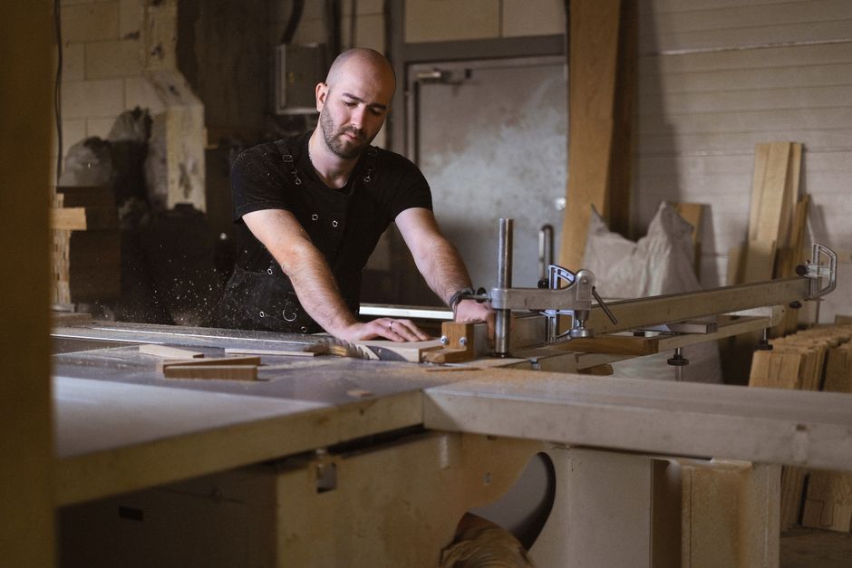 Skilled bearded male master cutting piece of wood with metal circular saw while working in professional joinery with special equipment