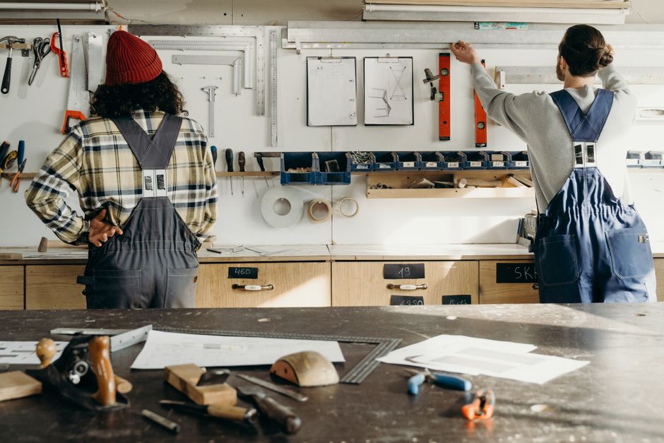 Two craftsmen in a workshop, organizing tools on a wall. Indoor carpentry scene.