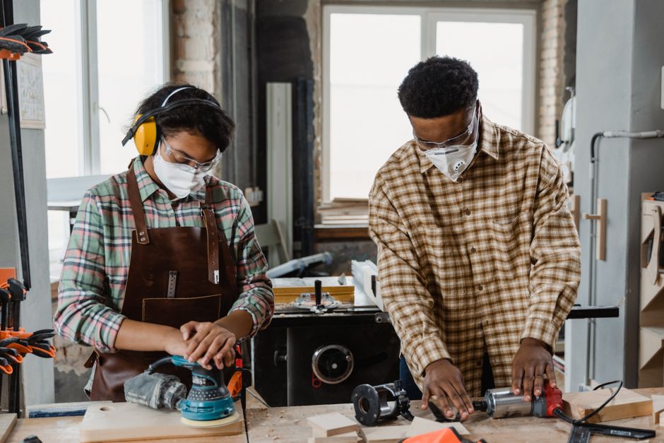 Two craftsmen wearing protective gear working with tools in a workshop.