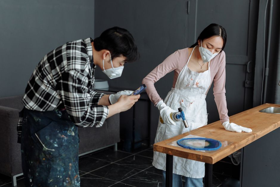 Two craftspeople working with wood and resin in an indoor studio setting.