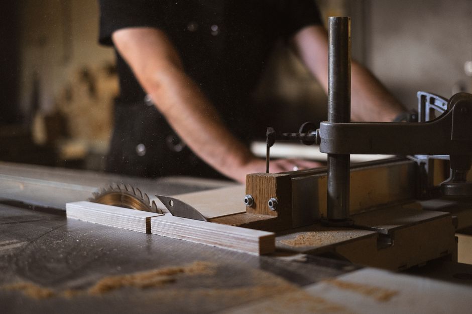 Unrecognizable blurred male carpenter cutting wooden details at sawbench with sharp knives while working in professional joinery with special instruments