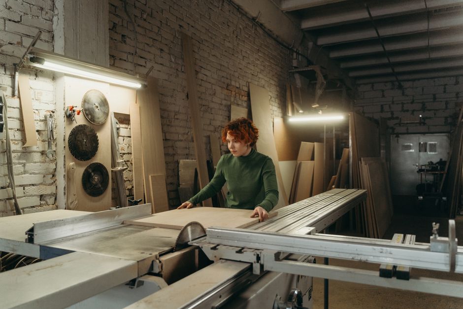Woman working with wood on a table saw in a carpentry workshop.