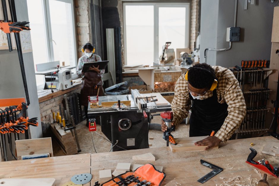 A carpenter using power tools in an indoor woodworking workshop, wearing safety gear.