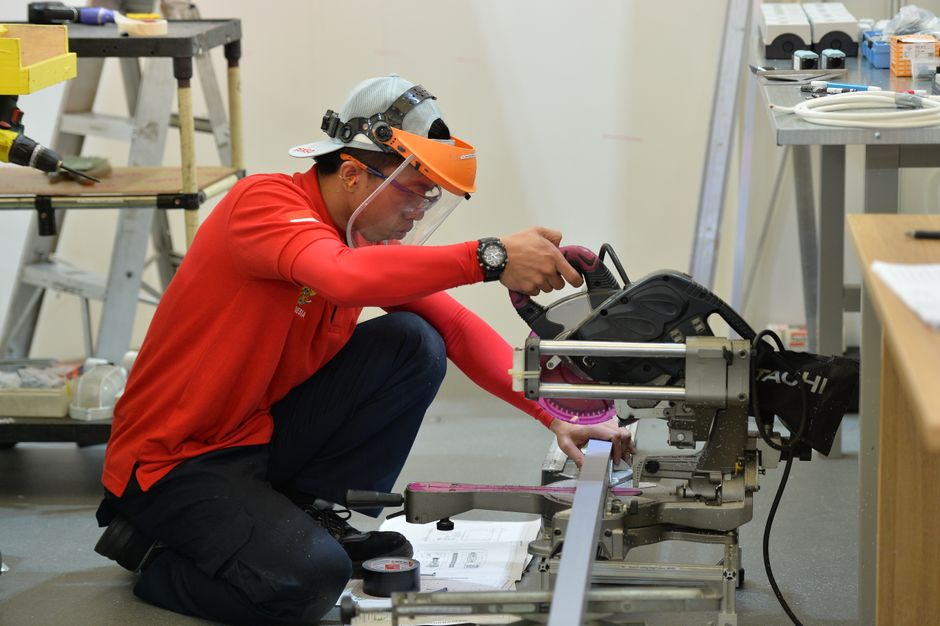 A focused construction worker operates a table saw while wearing protective gear inside a workspace.