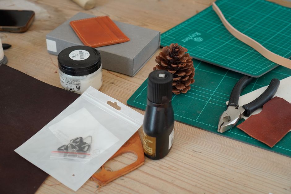 A variety of leather crafting tools and materials laid out on a wooden workbench.