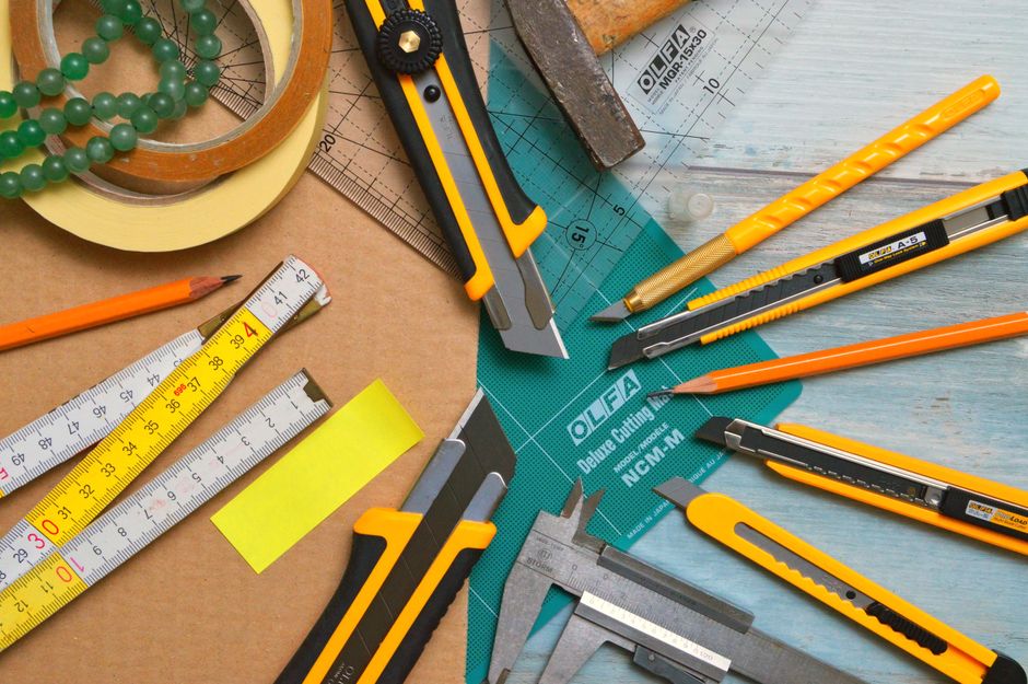 A vibrant flat lay of various office and craft tools, including knives and tapes, on a wooden surface.