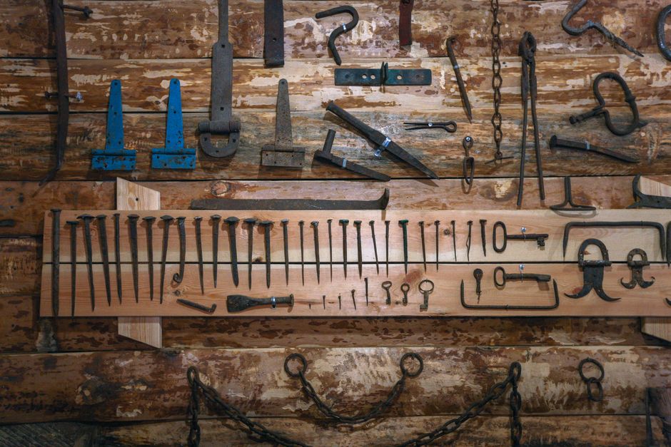 An array of vintage tools and nails displayed on a rustic wooden wall, showcasing craftsmanship history.