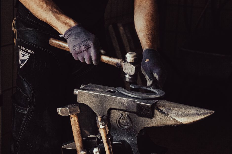 Close-up of a blacksmith forging a horseshoe indoors with tools.