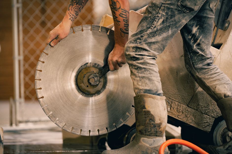 Close-up of a tattooed worker using a diamond saw, showcasing precision and skill in industrial work.