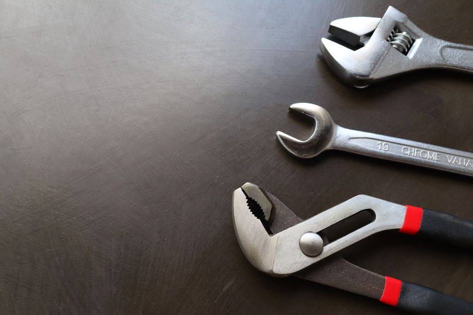 High-quality image of various metal tools including wrenches and pliers arranged on a dark surface.