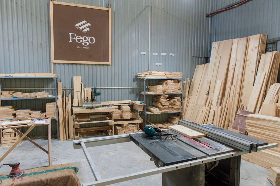 Interior of a wood workshop featuring a table saw, lumber stacks, and carpentry tools in an organized industrial setting.
