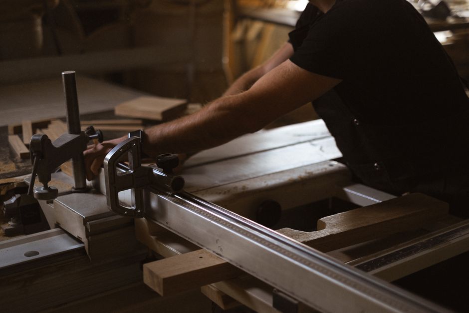 Side view of unrecognizable male master using metal sharp circular table saw while cutting wooden detail in workshop on blurred background