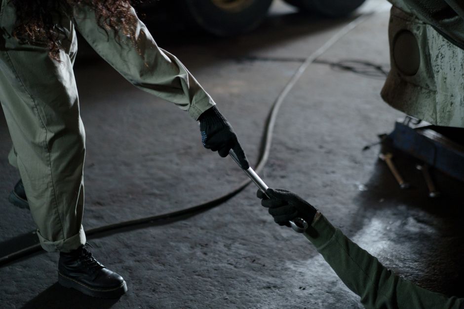 Two mechanics exchanging a wrench in a workshop, highlighting teamwork and skill.